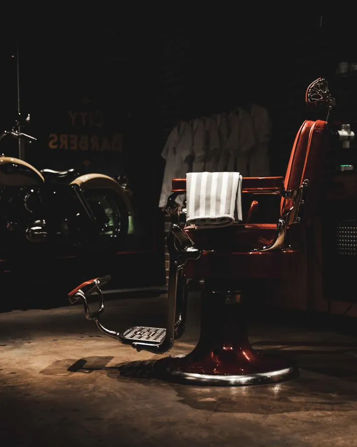 A red barber chair in the darkened shop, lit by a single light
