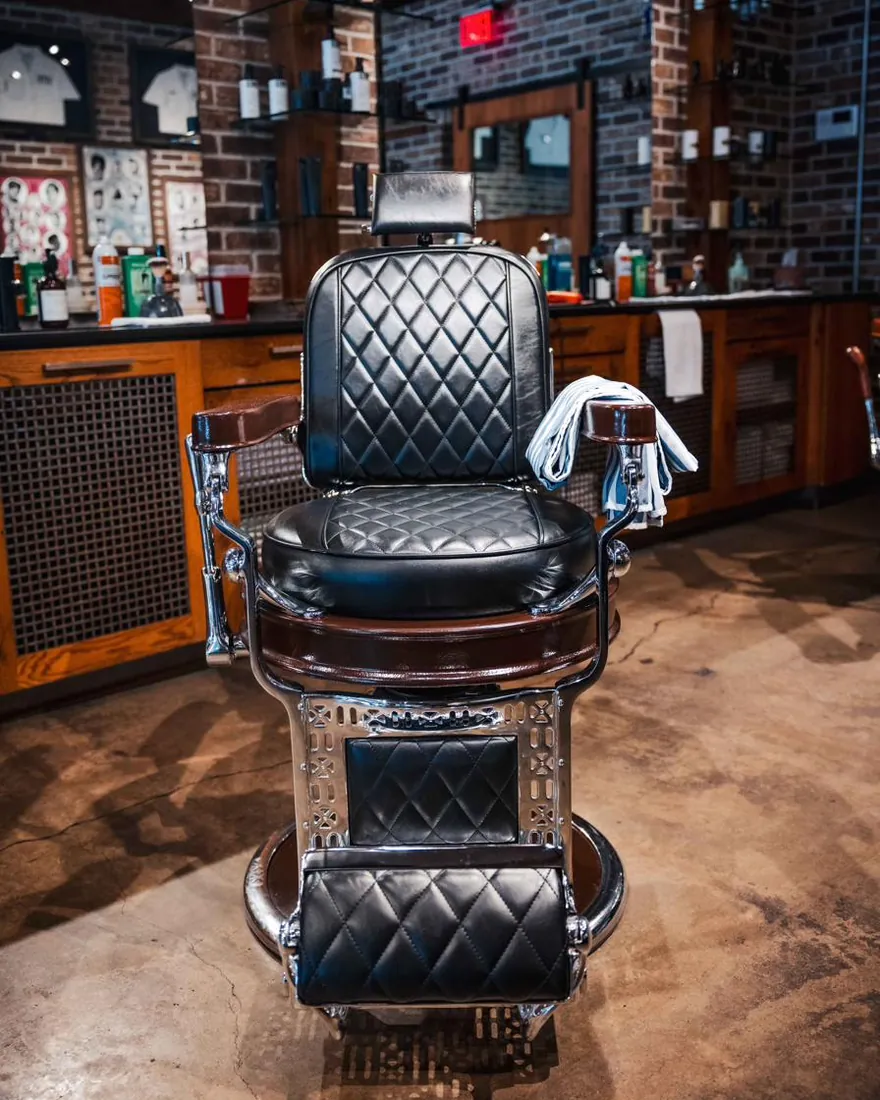 A black leather barber chair with a towel over the arm