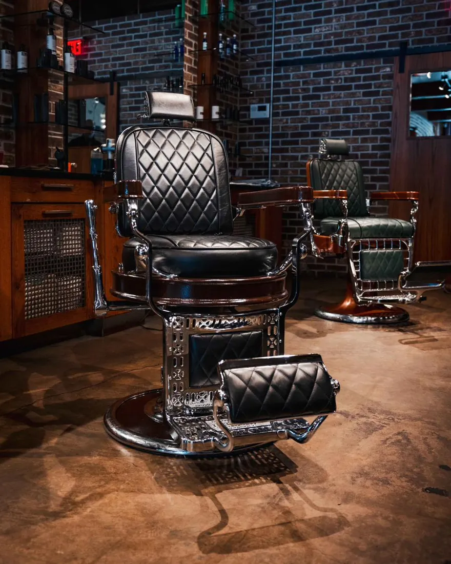 A black barber chair in front of a green leather chair on the shop floor