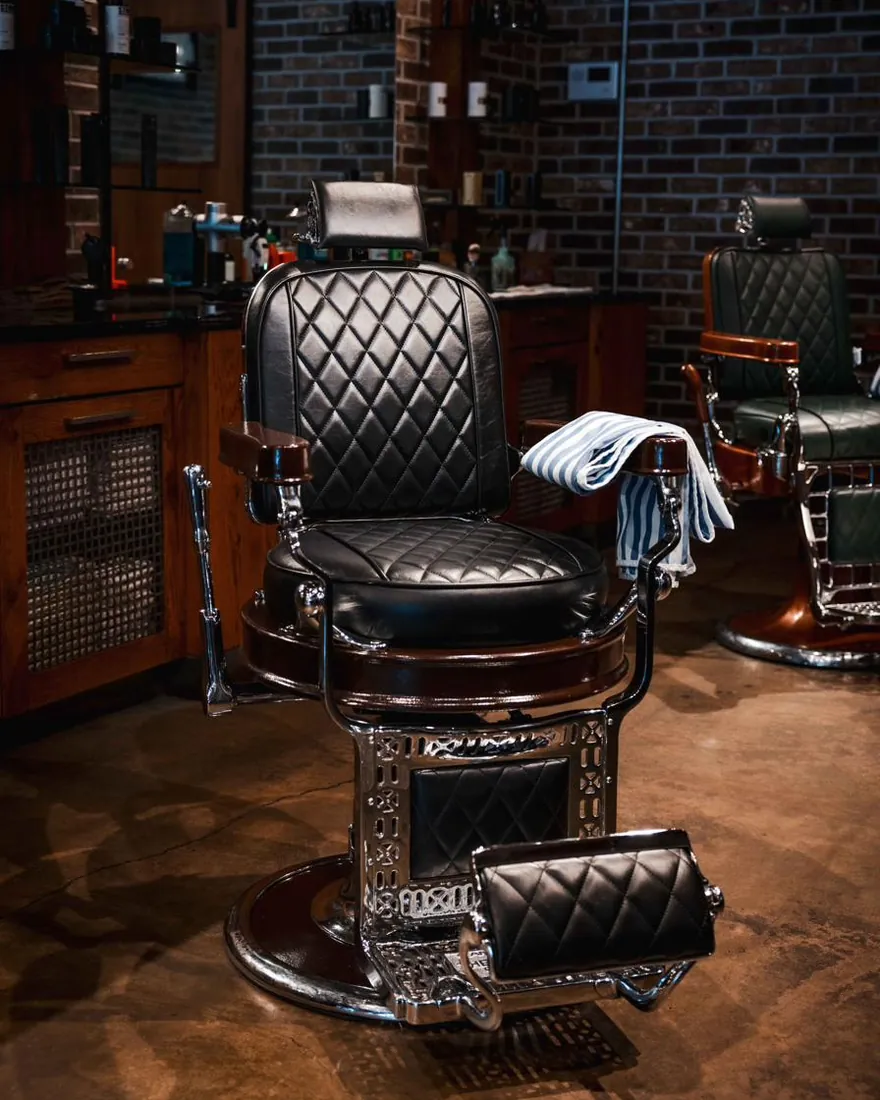 A black tufted barber chair with a towel on the arm