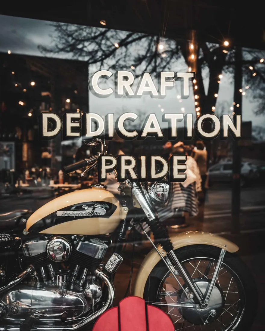 Gold “Craft, Dedication, Pride” lettering on the City Barbers window above a vintage motorcycle