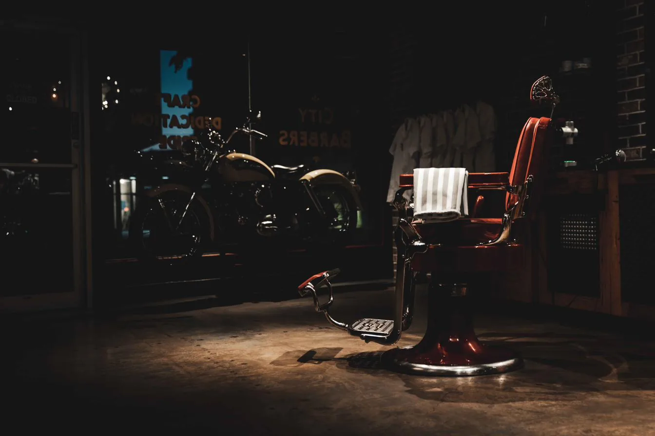 A red leather barber chair under a single light inside City Barbers